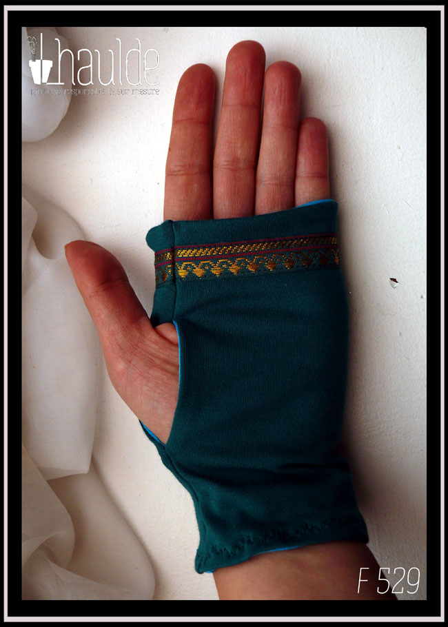 Mitaines en jersey bleu pétrole avec un galon au niveau des phalanges Il fait environ 15mm de large, fond bleu paon foncé, motifs dorés abstraits qui évoquent des pointes de flèches et deux lignes pourpres Vue de la paume