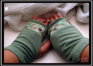 Mitaines en jersey vert d'eau avec un galon brodé au niveau des phalanges, il mesure 3 cm de large, fond vert turquoise pâle, losanges en fil doré avec au centre des cercles roses ou bleus ou rouge bordeaux et entre les pointes des losanges de petits sequins ronds dorés et des points de la même couleur que les cercles Vue de la paire vue de dessus, portée