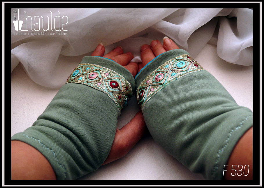 Mitaines en jersey vert d'eau avec un galon brodé au niveau des phalanges, il mesure 3 cm de large, fond vert turquoise pâle, losanges en fil doré avec au centre des cercles roses ou bleus ou rouge bordeaux et entre les pointes des losanges de petits sequins ronds dorés et des points de la même couleur que les cercles Vue de la paire vue de dessus, portée
