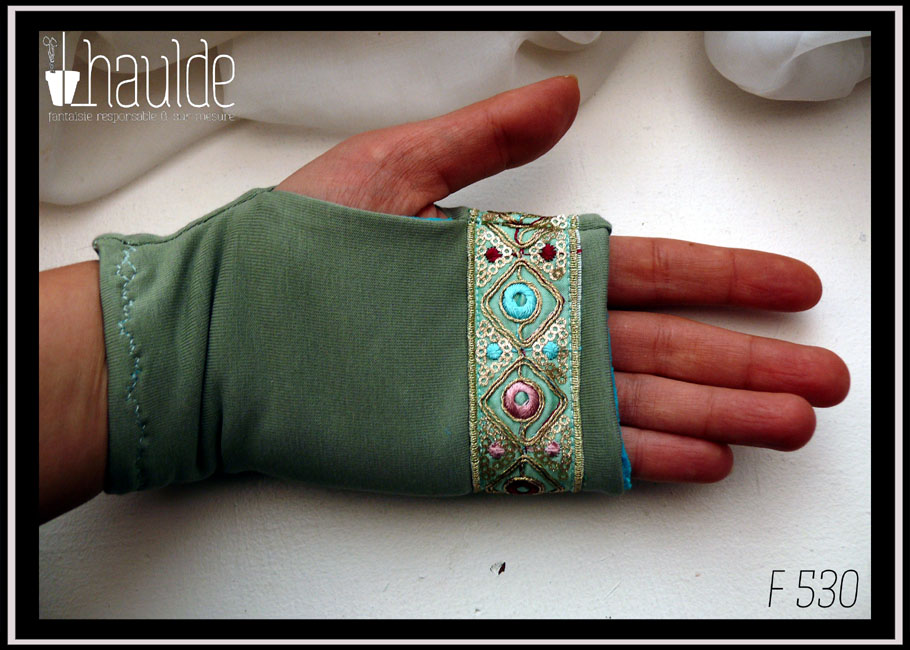 Mitaines en jersey vert d'eau avec un galon brodé au niveau des phalanges, il mesure 3 cm de large, fond vert turquoise pâle, losanges en fil doré avec au centre des cercles roses ou bleus ou rouge bordeaux et entre les pointes des losanges de petits sequins ronds dorés et des points de la même couleur que les cercles Vue de la paume