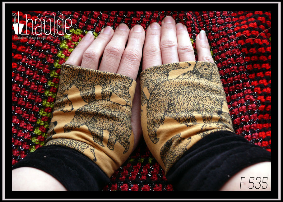 mitaines en jersey ocre imprimé ours dessinés à la plume, manchettes en velours noir Vue de la paire portée, de dessus, sur un coussin en crochet rouge et noir