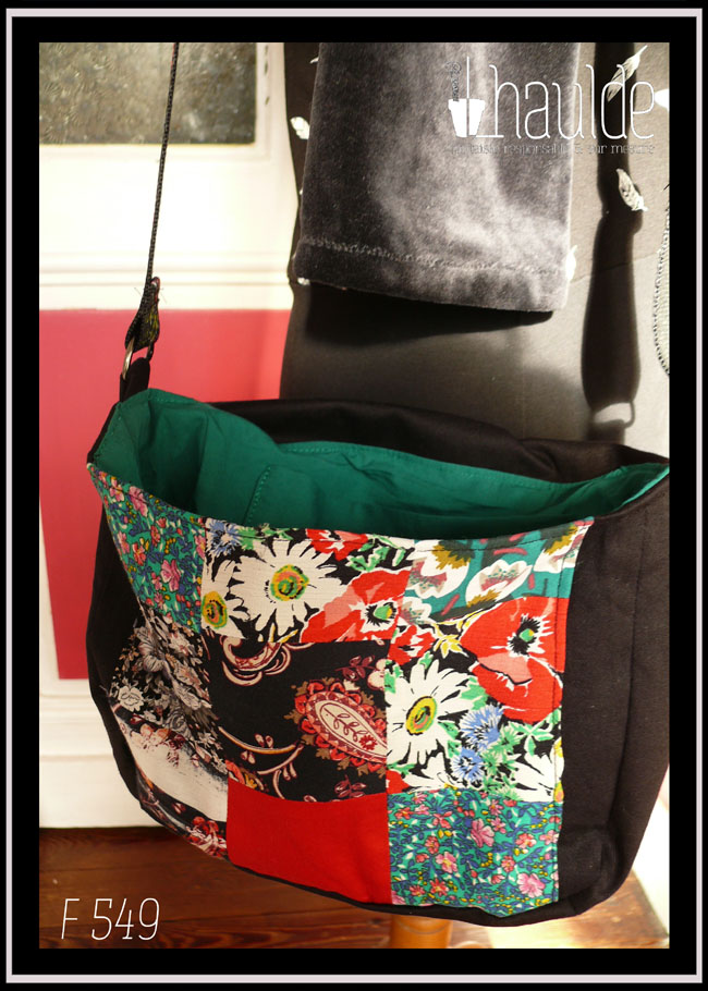 Sac à rabat en sergé noir, bords arrondis, bandoulière réglable sangle noire fleurie, avec sur le devant et sur le rabat un patchwork de carrés aux motifs fleuris, tons rouges et verts dominants. Vu ouvert Intérieur du sac en popeline vert émeraude