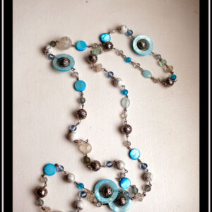 long collier de perles de verre, howlite, métal et nacre, assemblées par des tiges d'acier. Les perles alternent en format et en teinte (blanc et bleu)
