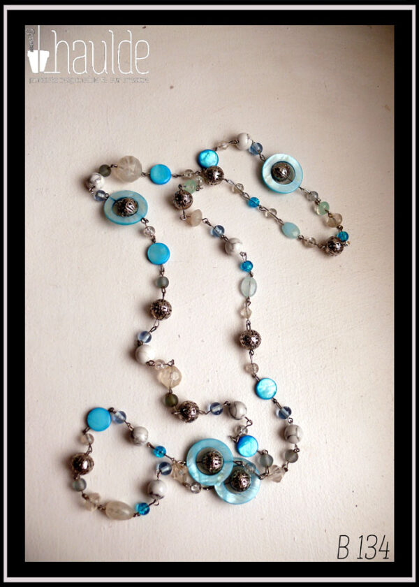 long collier de perles de verre, howlite, métal et nacre, assemblées par des tiges d'acier. Les perles alternent en format et en teinte (blanc et bleu)