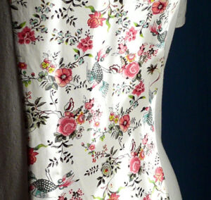 détail du tissu de la robe à manches courtes en maille pointelle blanche, centre en jersey imprimé motif fleurs roses et paons