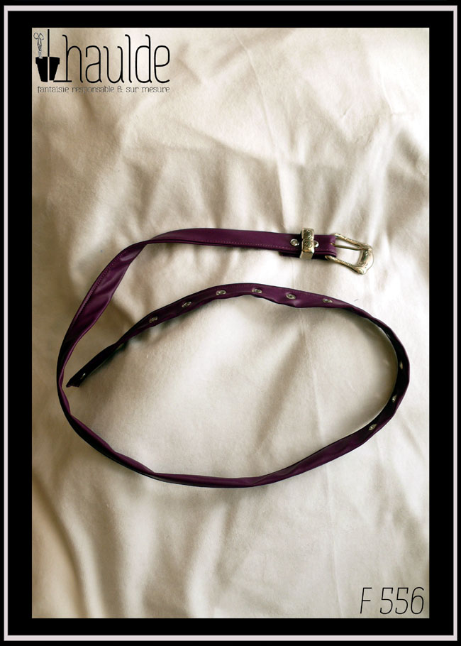 Ceinture en simili cuir violet, boucle rectangulaire en acier martelé (motifs arabesques végétales) Des oeillets d'acier protège les trous. Vue posée sur du velours blanc