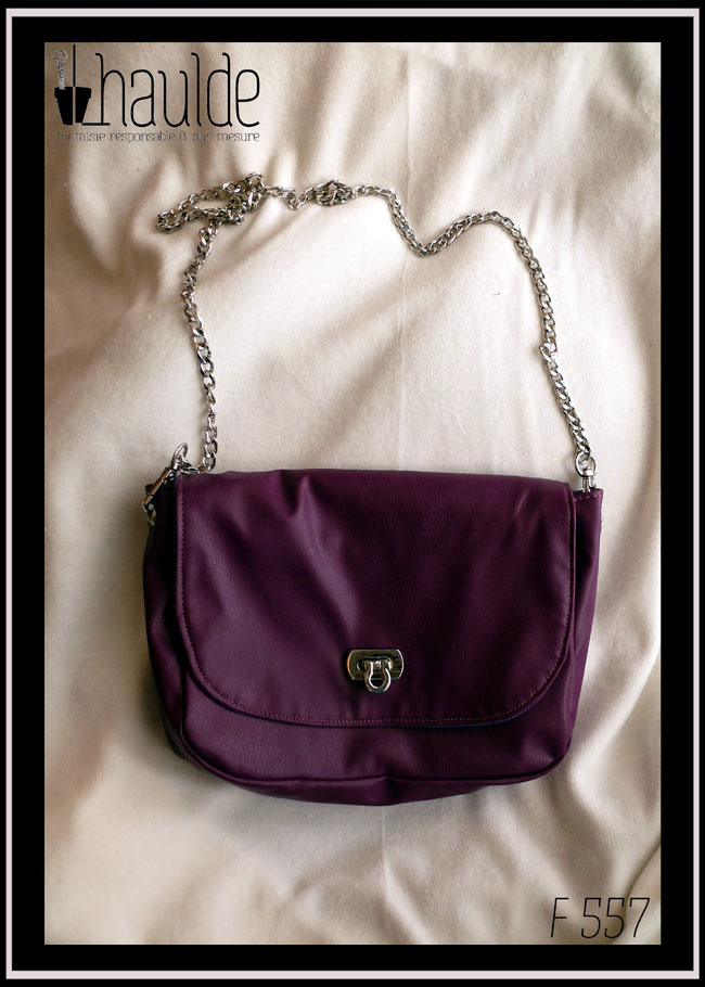 Petit sac à bandoulière chaine d'acier en simili cuir violet, rabat arrondi, fermoir pivotant en acier Vu posé sur du velours blanc