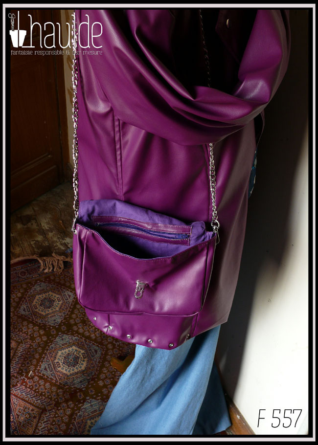 Petit sac à bandoulière chaine d'acier en simili cuir violet, rabat arrondi, fermoir pivotant en acier Vu ouvert, poche intérieure zippée apparente, sur un mannequin de couture qui porte une veste assortie dans la même matière
