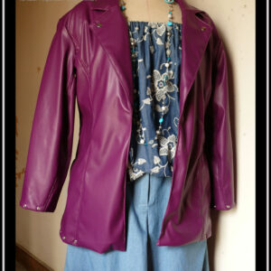 Veste en simili cuir, coupe ajustée, manchettes et bas de la veste garni d'oeillets en acier Vu sur un mannequin de couture qui porte également un haut en jean brodés de fleurs en dentelle blanche et un jean ample