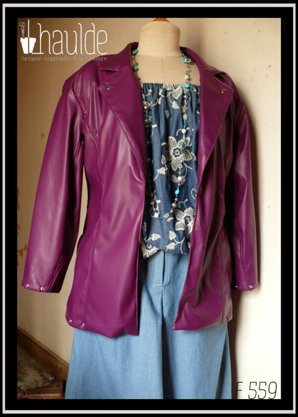 Veste en simili cuir, coupe ajustée, manchettes et bas de la veste garni d'oeillets en acier Vu sur un mannequin de couture qui porte également un haut en jean brodés de fleurs en dentelle blanche et un jean ample