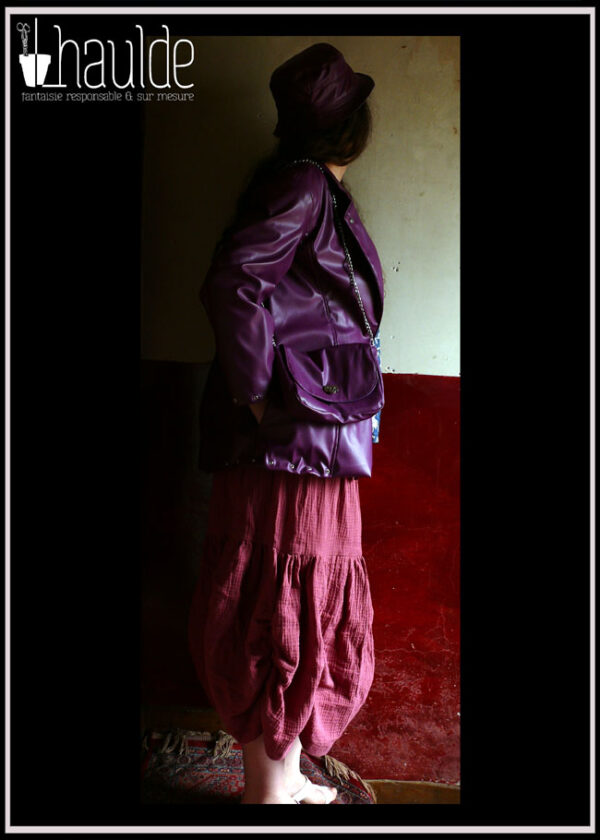 Bob en simili cuir violet, veste dans le même matériau, sac à bandoulière chaine en métal dans le même simili, jupe en double gaze mauve Le tout porté par une femme qui détourne la tête
