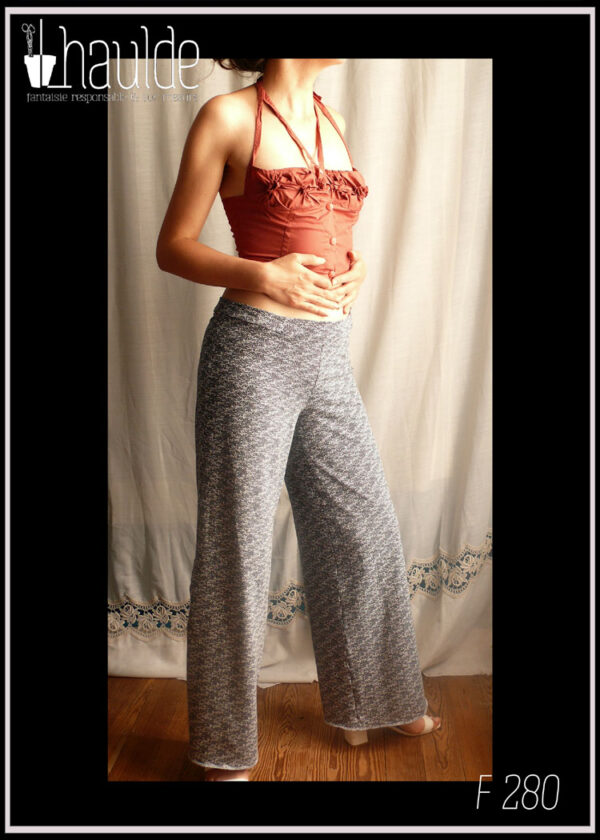 Femme debout portant un pantalon taille basse en jersey bleu foncé imprimé graphique blanc, jambes amples. Ainsi qu'un haut bustier en popeline rouille