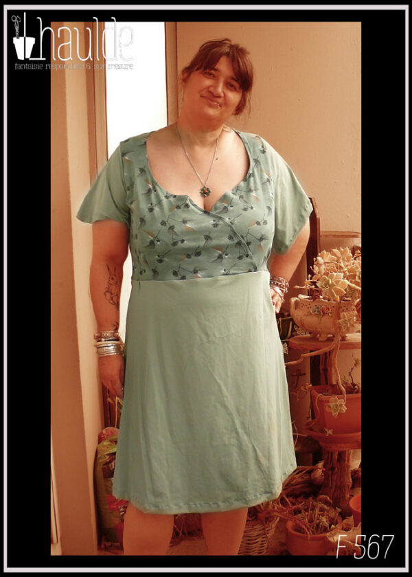 Robe manches courtes, coeur croisé, mi-longue, en jersey. Coeur croisé fond vert céladon imprimé fleurs stylisées façon plumeaux, manches et jupe en vert céladon uni vue portée de face par une dame