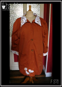 Manteau en sergé roux, col et manchettes blanches imprimé ginkgo, le même imprimé est découpé et appliqué en bas du pan avant droit Deux grandes poches plaquées, deux boutons Vu de face sur un mannequin de couture