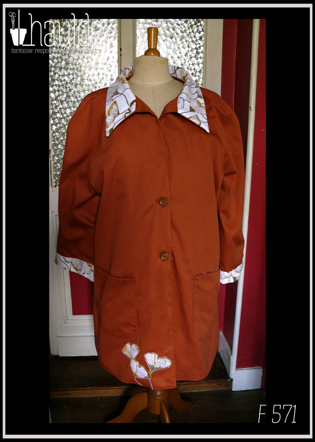 Manteau en sergé roux, col et manchettes blanches imprimé ginkgo, le même imprimé est découpé et appliqué en bas du pan avant droit Deux grandes poches plaquées, deux boutons Vu de face sur un mannequin de couture