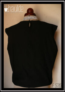 Haut sans manche en french terry noir, ras du cou, façon blouse avec un bas élastiqué qui renforce l'aspect bouffant vu de dos sur un mannequin de couture, il y a une petite fente au niveau du coup pour permettre un enfilage plus facile (se ferme avec un crochet)
