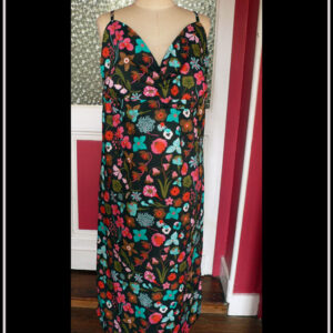 Robe dos nu en popeline noire imprimé fleurs à dominante rose-rouge et turquoise Décolleté en V courbe, bretelles fines Vue de face sur un mannequin de couture