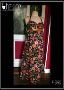 Robe longue dos nu, bretelles nouées au cou en tissu Liberty™ noir imprimé motifs fleuris et petits pois dorés Une bande élastique dorée ceint la robe sous la poitrine Vue de face sur un mannequin de couture
