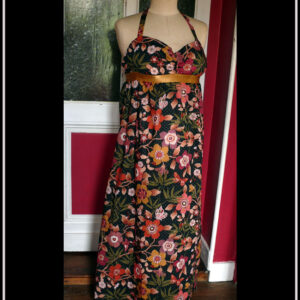 Robe longue dos nu, bretelles nouées au cou en tissu Liberty™ noir imprimé motifs fleuris et petits pois dorés Une bande élastique dorée ceint la robe sous la poitrine Vue de face sur un mannequin de couture