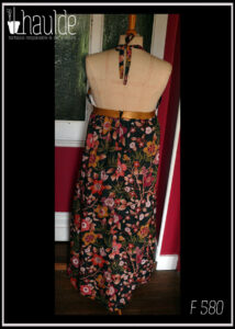 Robe longue dos nu, bretelles nouées au cou en tissu Liberty™ noir imprimé motifs fleuris et petits pois dorés Une bande élastique dorée ceint la robe sous la poitrine Vue de face sur un mannequin de couture