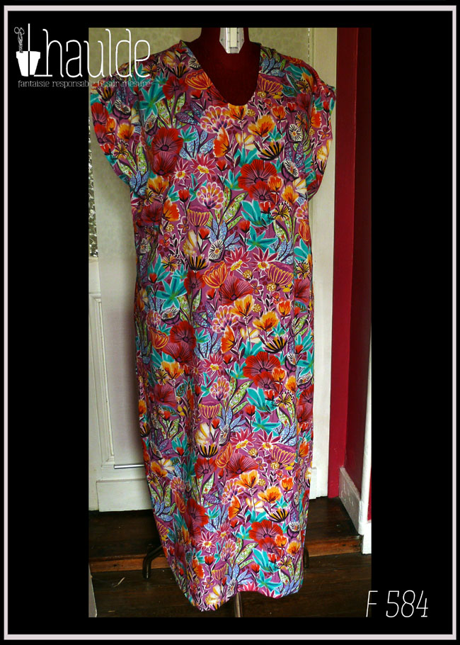 Robe longue manches très courtes en tissu imprimé fleurs stylisées multicolores (dominante rose et orange-rouge) et feuillage turquoise sur fond rose. Vue de face sur un mannequin de couture . Encolure en V arrondi