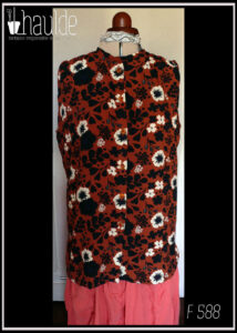 Haut sans manches, froncé aux épaules en viscose terracotta imprimée fleurs blanches et silhouettes de fleurs et feuilles noires Boutons en résine contenant des fleurs séchées oranges. Col à liseret simple Vu de face sur un mannequin de couture