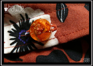 gros plan d'un des boutons en résine contenant des pétales de fleurs oranges et de la feuille d'or froissée