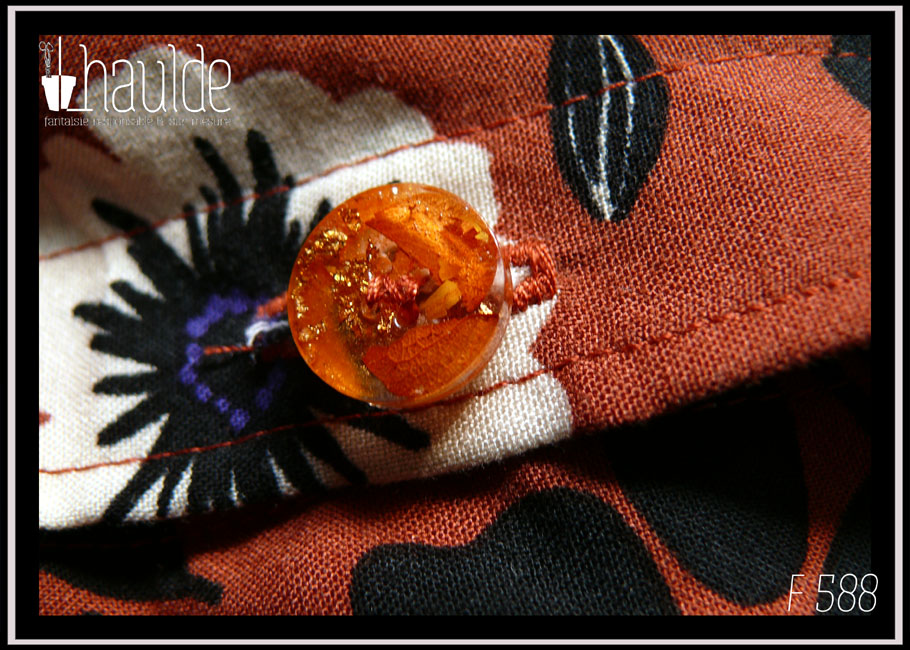 gros plan d'un des boutons en résine contenant des pétales de fleurs oranges et de la feuille d'or froissée