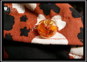 gros plan d'un des boutons en résine contenant des pétales de fleurs oranges et de la feuille d'or froissée