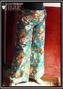 Pantalon ample en coton vert canard imprimé de camélia japonais blancs, vermillon, or et bleus cernés d'or Il est noué des deux côté à la taille, ici avec les pans de la ceinture qui sont noués court Vu porté, de face