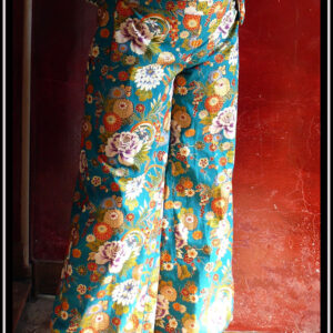 Pantalon ample en coton vert canard imprimé de camélia japonais blancs, vermillon, or et bleus cernés d'or Il est noué des deux côté à la taille, ici avec les pans de la ceinture qui sont noués court Vu porté, de face