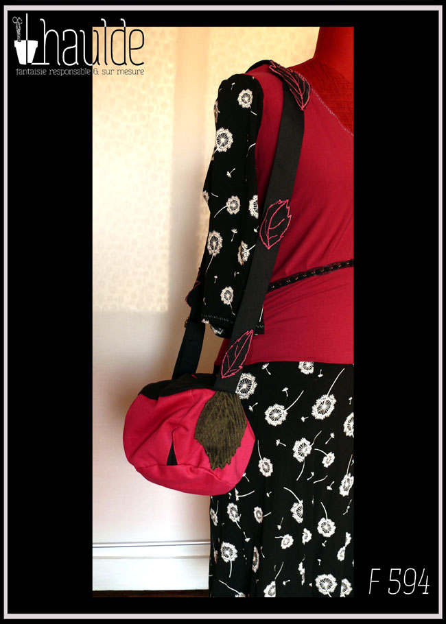 sac boule à bandoulière, vu suspendu à l'épaule d'un mannequin de couture Fond rose fuchsia, dessus et bandoulière en sergé noir Bandoulière garnie de feuilles de sergé noir à nervures rose, feuilles en velours côtelé kaki plaquée sur le sac