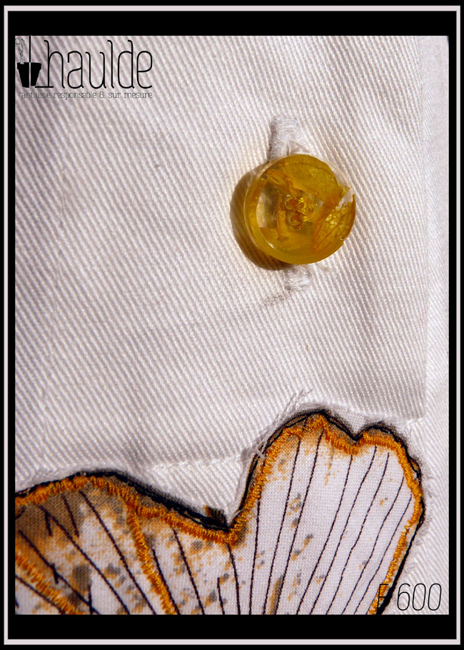 détail d'un bouton en résine avec des fleurs jaunes incrustées dedans, en dessous le haut d'une feuille de ginkgo appliquée (tissu imprimé)