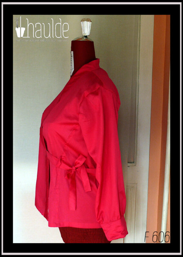 Chemisier croisé sur le devant, noué côté gauche, à manches longues en satin rose vif. Col châle plat Vu de profil sur un mannequin de couture. Profil gauche, on voit le noeud au niveau de la taille