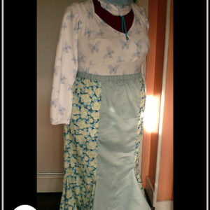 Jupe longue à taille élastique et à double quilles en bas en coton bleu imprimé petites fleurs de cerisiers blanches. Au centre devant il y a un pan de satin bleu pâle. La ceinture est dans la même matière Haut manches longues coeur croisé en jersey blanc imprimé papillons bleus translucides Il y a une légère fronce de chaque côté sous les épaules et les manchettes sont élastiquées Vu de trois quarts face sur un mannequin de couture réglé sur la taille 52. Le haut est très moulant et passe sous la jupe Un macaron en bas à gauche indique que la photo a été prise sur un mannequin de couture réglé en taille 52