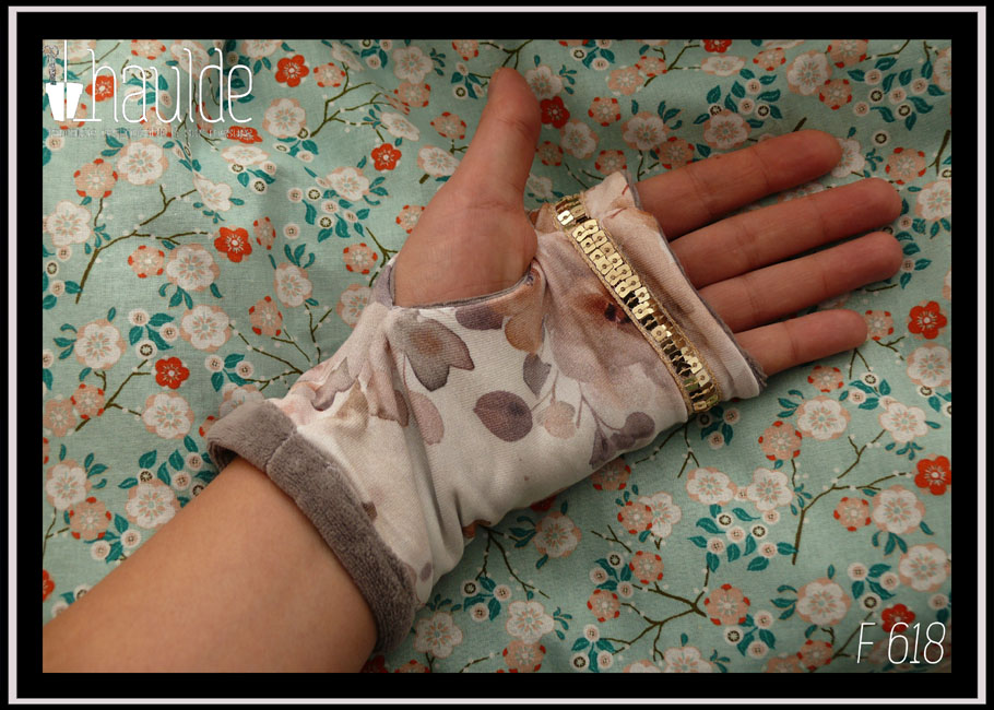 Mitaines en jersey blanc imprimé fleurs aquarellées dans les tons oranges-gris. Manchettes en velours gris. Un galon de sequins carrés dorés sur deux rangs décore au niveau des phalanges Vue d'une mitaine portée côté paume