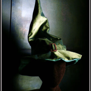Chapeau de sorcière à haut bout pointu et large rebord en velours vert foncé avec un ruban du même velours et une boucle de ceinture au centre en acier couleur bronze Vu porté par une tête de mannequin