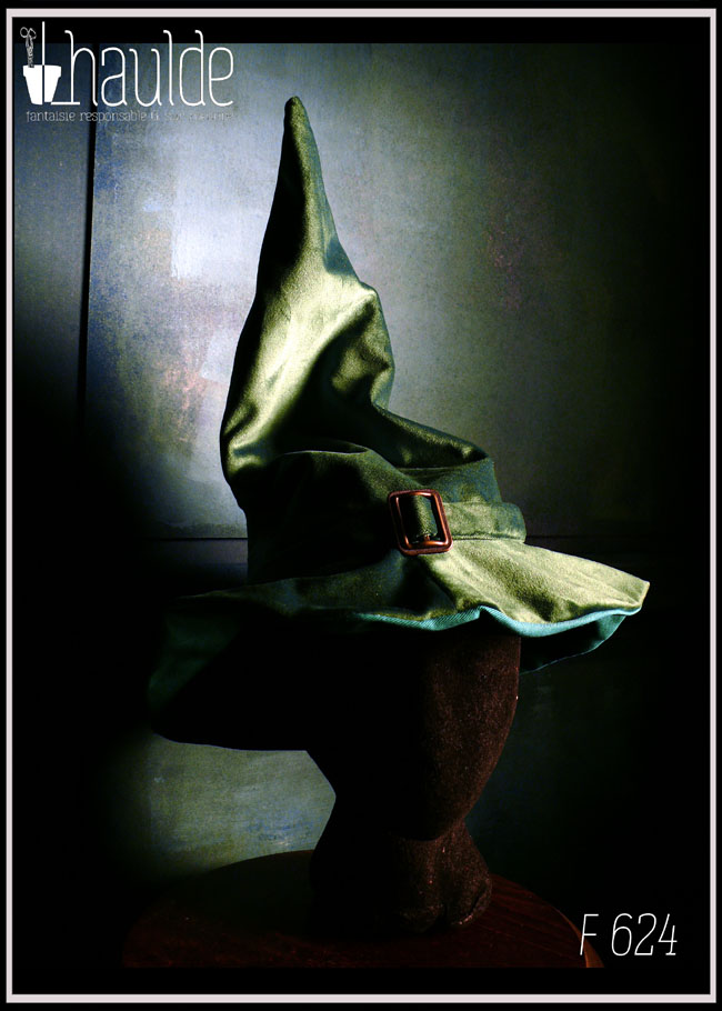 Chapeau de sorcière à haut bout pointu et large rebord en velours vert foncé avec un ruban du même velours et une boucle de ceinture au centre en acier couleur bronze Vu porté par une tête de mannequin