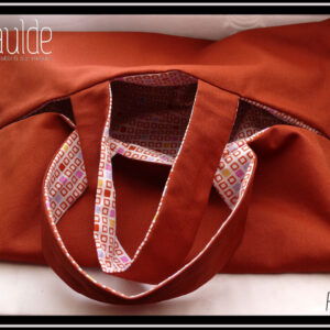 Sac à tarte, rectangle fendu tout du long au milieu avec deux anses centrales de chaque côté de la fente, extérieur couleur terracotta, intérieur blanc motifs petits carrés terracotta, certains pleins, jaunes, rose, mauve Vu entrouvert