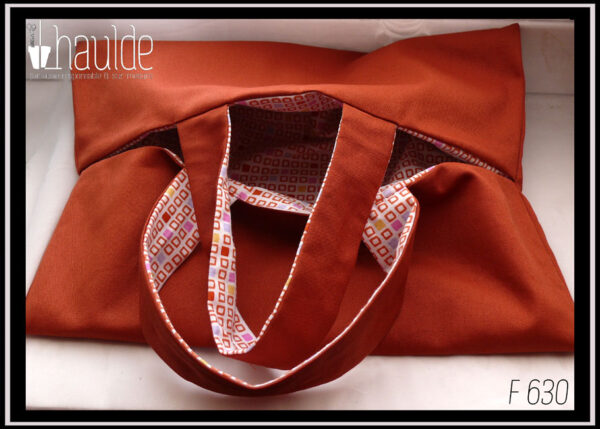 Sac à tarte, rectangle fendu tout du long au milieu avec deux anses centrales de chaque côté de la fente, extérieur couleur terracotta, intérieur blanc motifs petits carrés terracotta, certains pleins, jaunes, rose, mauve Vu entrouvert