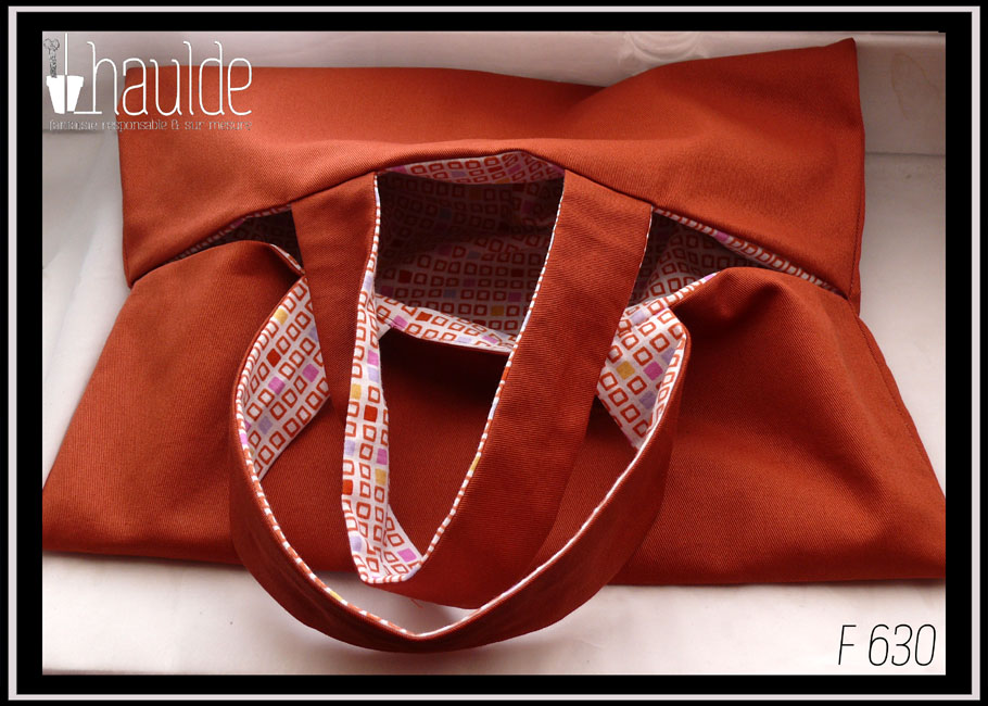 Sac à tarte, rectangle fendu tout du long au milieu avec deux anses centrales de chaque côté de la fente, extérieur couleur terracotta, intérieur blanc motifs petits carrés terracotta, certains pleins, jaunes, rose, mauve Vu entrouvert