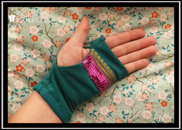 Mitaines en jersey bleu pétrole garnies au niveau de l'ouverture du pouce d'un galon brodé de doré et de pourpre (motifs abstraits) et d'un galon de 5 rangs de sequins carrés fuchsia Vue de la paire portée côté paume