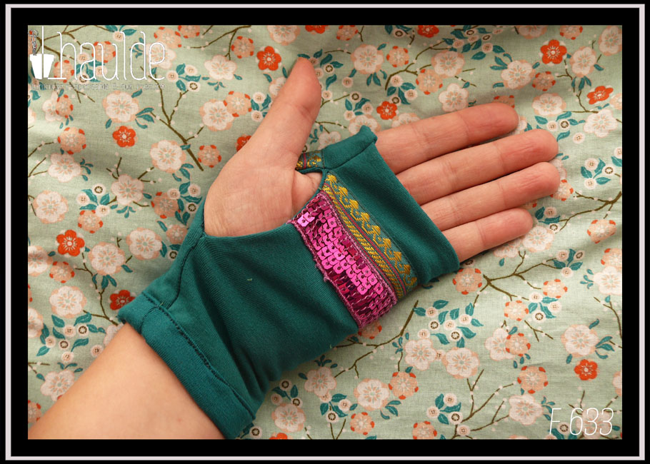 Mitaines en jersey bleu pétrole garnies au niveau de l'ouverture du pouce d'un galon brodé de doré et de pourpre (motifs abstraits) et d'un galon de 5 rangs de sequins carrés fuchsia Vue de la paire portée côté paume