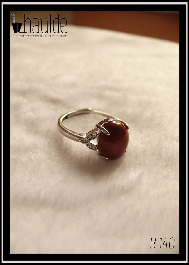 Bague avec un petit cabochon ovale en jaspe rouge monté sur un support en argent garni de chaque côté de trois petites mandorles contenant des éclats d'oxyde de zirconium Vue sur fond blanc, la pierre est opaque