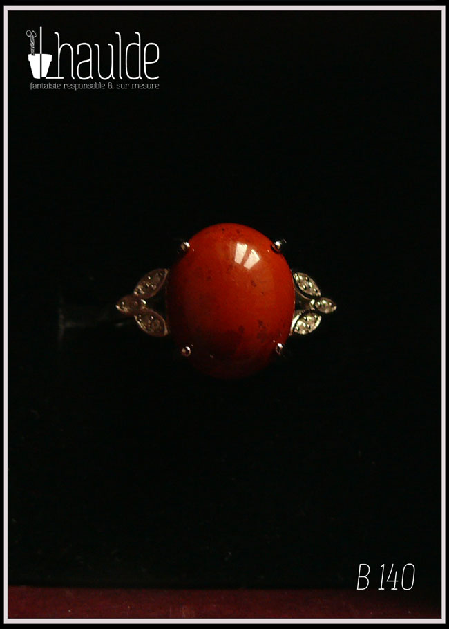 Bague avec un petit cabochon ovale en jaspe rouge monté sur un support en argent garni de chaque côté de trois petites mandorles contenant des éclats d'oxyde de zirconium Vue sur fond noir