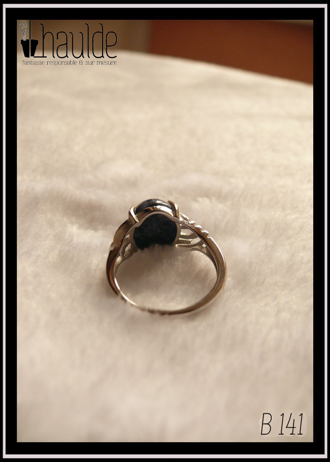 Bague avec un petit cabochon ovale en sodalite, pierre bleu foncé marbré de bleu nuit, montée sur un support en argent dont les côtés sont ajourés. Vue de dos sur un fond blanc, l'anneau est ajustable