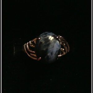 Bague avec un petit cabochon ovale en sodalite, pierre bleu foncé marbré de bleu nuit, montée sur un support en argent dont les côtés sont ajourés. Vue de dessus sur un fond noir
