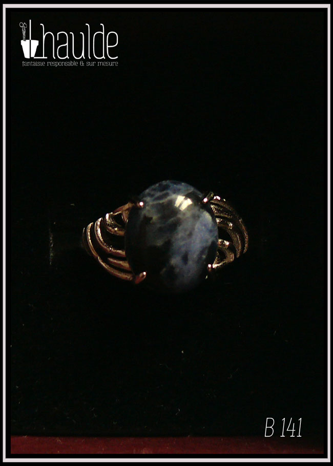 Bague avec un petit cabochon ovale en sodalite, pierre bleu foncé marbré de bleu nuit, montée sur un support en argent dont les côtés sont ajourés. Vue de dessus sur un fond noir
