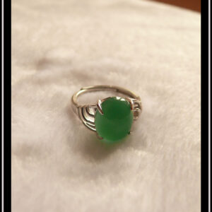 Bague avec un petit cabochon ovale en aventurine vert foncé montée sur un support en argent dont les côtés sont ajourés. Vue sur fond blanc, de face, la pierre est translucide