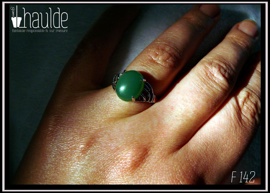 Bague avec un petit cabochon ovale en aventurine vert foncé montée sur un support en argent dont les côtés sont ajourés. Vue portée sur un annulaire au soleil